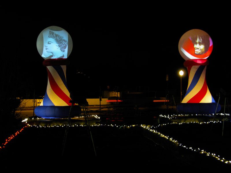Projections of two people's heads onto the spheres of two, giant, inflatable barber shop polls.